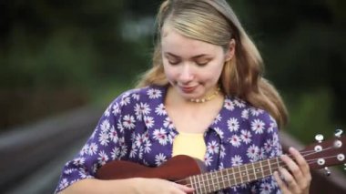 Genç çekici kız gitar çalar. Güzel kız gün batımında mor bir gömlekle Ukulee çalıp şarkı söylüyor. Gitarla köprüde oturan hippi.