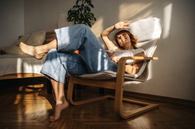 Güzel bir kız kanepede uzanıyor ve kafasının üstünde kitap okuyor.