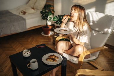 Mutfakta bir fincan kahve ve kruvasanla güzel genç bir kadın..