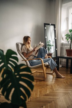 Kanepede oturup kitap okuyan güzel genç bir kadın.