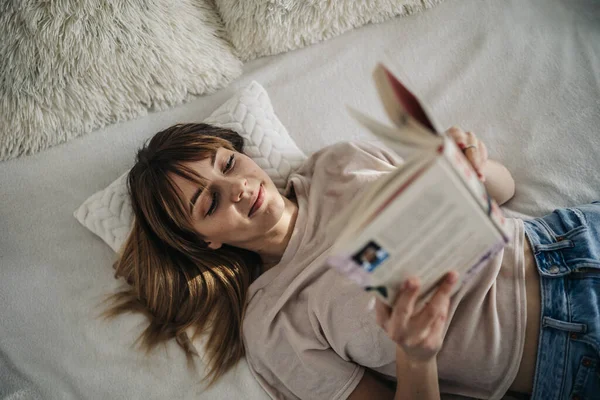 Evdeki kanepede kitap okuyan genç bir kadın.