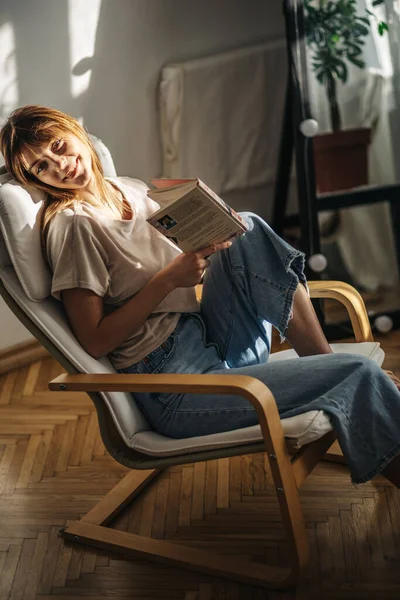 Kanepede oturup kitap okuyan güzel genç bir kadın.