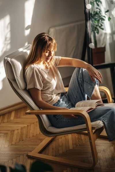 Kanepede oturup kitap okuyan güzel genç bir kadın.