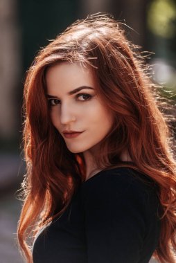 Siyah elbiseli güzel, kızıl saçlı, stil sahibi bir kız. Şehir sokaklarında ilkbaharda uzun saçlı, zarif bir kadın portresi..