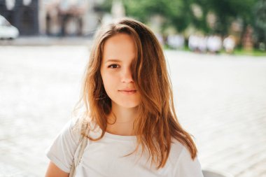 Arka planda yaz kıyafetleri içinde gülümseyen genç bir kızın portresi..