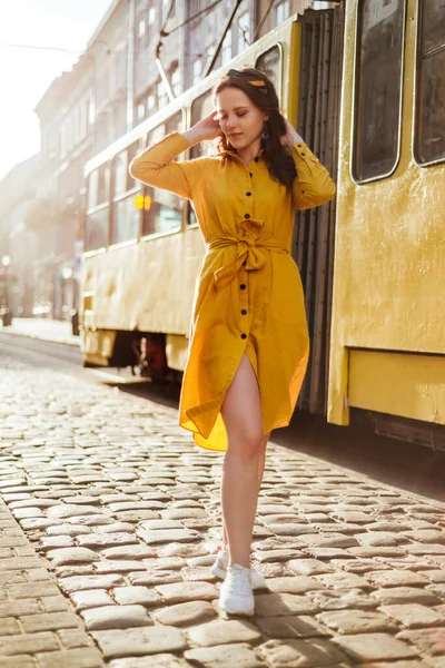 Eski şehir sokaklarında tramvayı olan sarı gömlekli şık bir kız. Genç kadın sabah saatlerinin yaz portresi