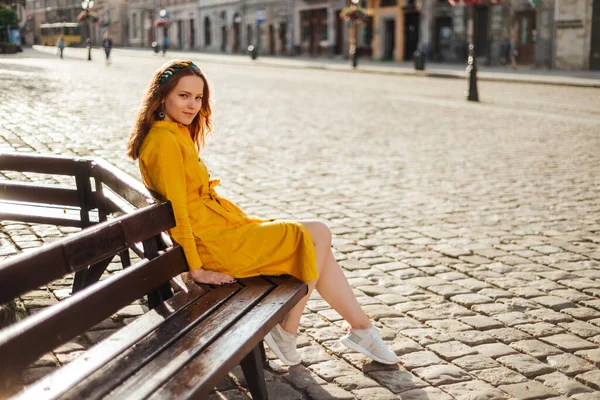 穿着黄色衬衫和白色运动鞋的时髦女孩坐在长椅上 年轻漂亮的女人在户外的夏季肖像 — 图库照片