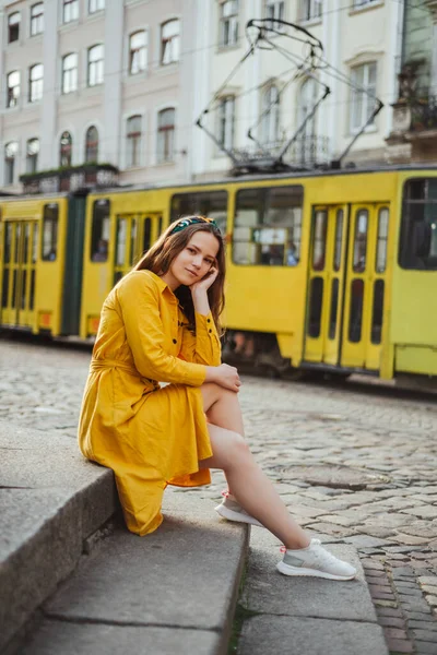 Yazlık gömlekli şık kız arka planda tramvayla eski taş merdivenlerde oturuyor. Sarı elbiseli kadın portresi