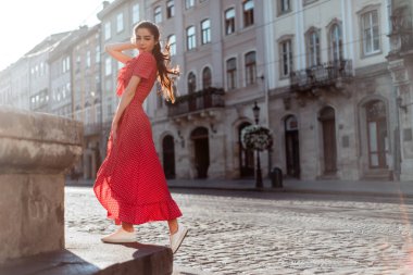 Eski şehir caddesinde yaz kıyafetleri içinde şık bir kız yürüyor. Yazın kırmızı elbiseli genç bir kadın portresi