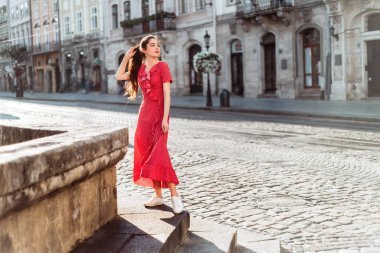 Kırmızı benekli elbiseli esmer kız. Eski şehrin arka planında retro kıyafetli kadın portresi