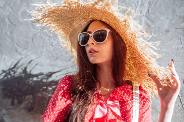 Hasır şapkalı şık bir kız. Güneşli bir günde kırmızı retro elbiseyle genç bir kadın portresi