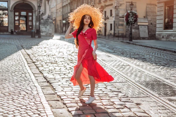 Kırmızı benekli elbisesi ve beyaz spor ayakkabıları olan hasır şapkalı yaz kızı. Yaz zamanı Çekici bir kadının gündüz portresi