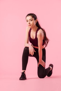 Pembe arka planda oturan tozlu ve spor elbiseli bir kız. Spor, aktif sağlıklı yaşam tarzı. Spor salonundaki kadın portresi.