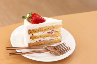 Çilekli ve kremalı kek beyaz tabakta bir kafedeki ahşap masada.