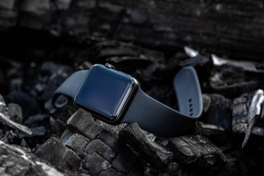 Kolun üzerinde modern bir elektronik saat kömürlerin üzerinde duruyor. Lastik kayışlı siyah saat..