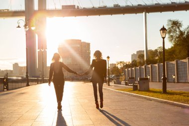 Sarı saçlı iki kız güneş ışığında sahil yolunda el ele yürüyorlar. LGBT topluluğunun temsilcileri.