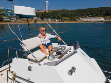 Kar beyazı bir yatın ikinci katında üst güvertede oturan bir kız. Kaptanlar köprüsü.