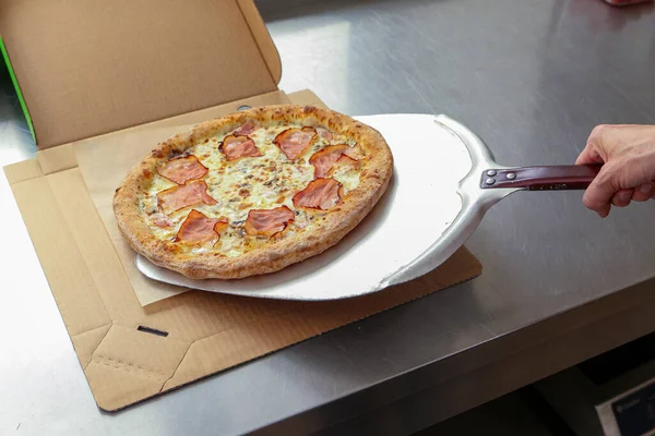Pizzaiollo folds the pizza from the pizza spatula onto the table where the corton box lies. Ordering, pizza delivery.