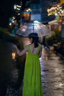 Genç Asyalı kadın gezgin geceleri şeffaf şemsiyeli fener tutuyor E-Thong köyü, Pilok madeni, Thong Pha Phum Ulusal Parkı, Kanchanaburi, Tayland