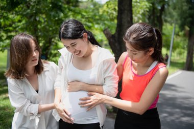 Two Asian women helping pregnant woman outdoor in the park, she was in pain because she was about to give birth