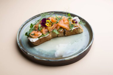 Çiçeklerle süslenmiş bir tostun üzerinde krem peynirli dilimlenmiş somon balığı.