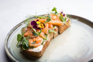 Çiçeklerle süslenmiş bir tostun üzerinde krem peynirli dilimlenmiş somon balığı.
