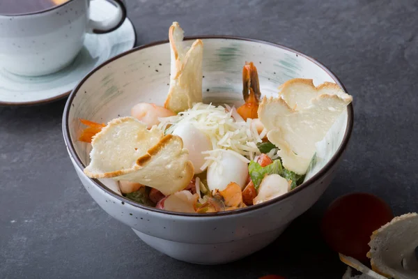 Bowl of shrimp caesar salad served for lunch on a cafe table