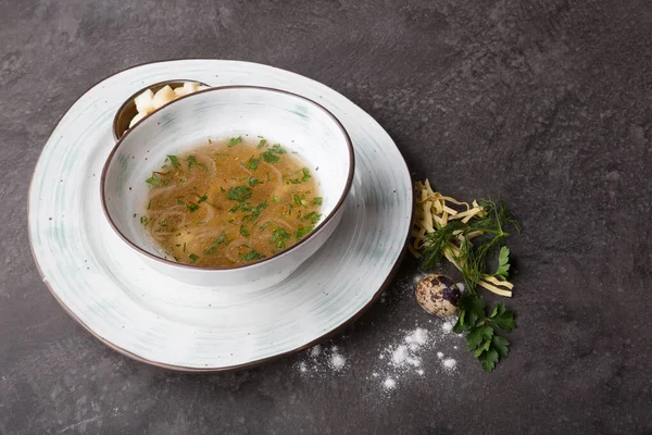 Bowl of pasta soup served with croutons and herbs on a cafe table