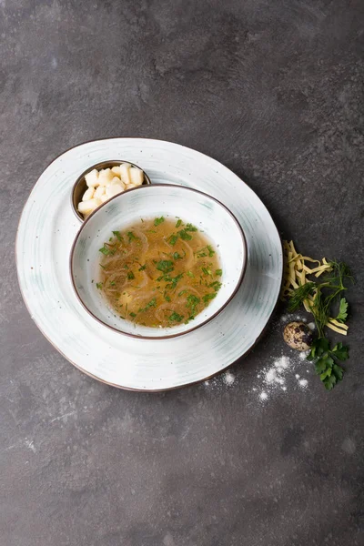 Bowl of pasta soup served with croutons and herbs on a cafe table