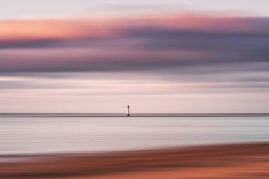 Lighthouse in seascape abstract with panning motion combined with a long exposure. Image displays soft, pastel colors in a retro style.