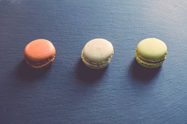 Koyu, karamsar bir çikolata, karamel ve vanilyalı badem kurabiyesinin koyu gri bir beton desenli arka planda sıralanması..