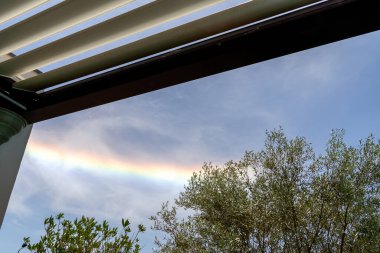 Colorful iridescent cloud, Beautiful Rainbow cloud over oliver trees and pergola La Rochelle France