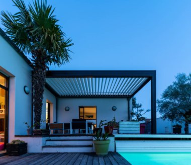 Modaya uygun teras pergola yapısı, tente ve teras çatısı, bahçe salonu, sandalyeler, peyzaj ile çevrili metal ızgara. İyi geceler.