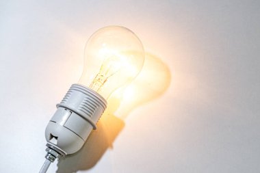 Ampul açık, beyaz bir yüzeyde, gölgesini beyaz yüzeyde bırakır.. 