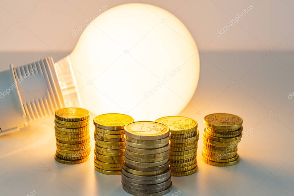 Lit light bulb with coins beside it. Increase in energy tariffs. Efficiency and energy saving. 