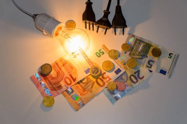Faturalar, paralar, banknotlar ve elektrik prizleriyle aydınlatılmış ampul. Enerji tarifeleri ve fiyatlarında artış. 