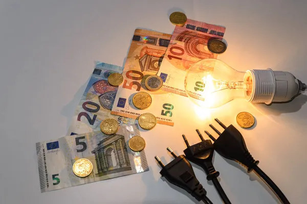Light bulb lit with bills, coins, banknotes and electric plugs. Increase in energy tariffs and prices.