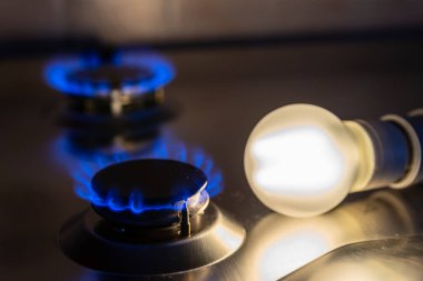 Yanında bozuk paralar olan gaz ocağının yanındaki ampulü yak. Enerji ve gaz masrafları, maliyet artışları. Yanı başında bozuk paralarla yanan bir ampul. Enerji ve gaz maliyetleri, maliyet artışı.