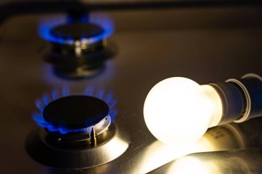 Yanında bozuk paralar olan gaz ocağının yanındaki ampulü yak. Enerji ve gaz masrafları, maliyet artışları. Yanı başında bozuk paralarla yanan bir ampul. Enerji ve gaz maliyetleri, maliyet artışı.