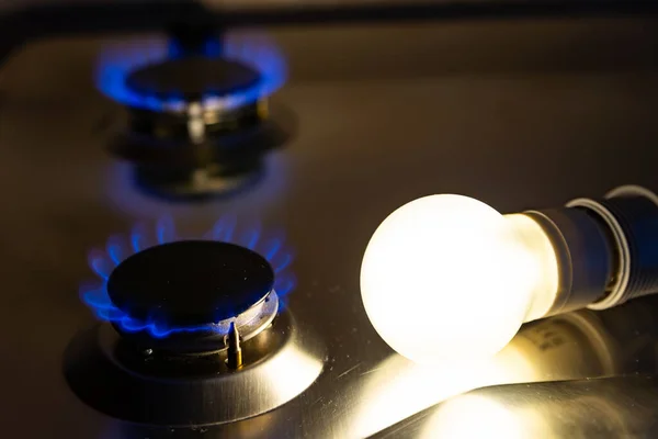 Light bulb on next to lit gas cooker, with coins next to it. Energy and gas costs, cost increases.Light bulb on next to lit gas cooker, with coins next to it. Energy and gas costs, cost increases.