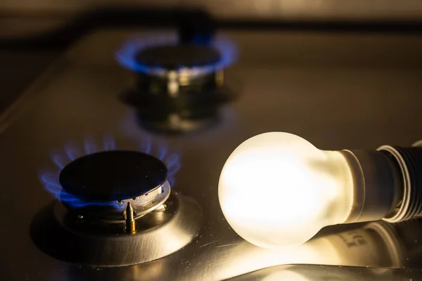 Light bulb on next to lit gas cooker, with coins next to it. Energy and gas costs, cost increases.Light bulb on next to lit gas cooker, with coins next to it. Energy and gas costs, cost increases.