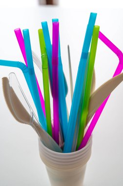 Plates, straws, knives, forks, glasses, disposable plastic objects, photographed closely. Plastic recycling and sales ban.