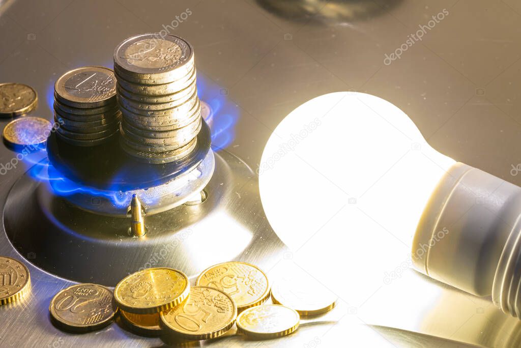 Light bulb on next to lit gas cooker, with coins next to it. Energy and gas costs, cost increases.