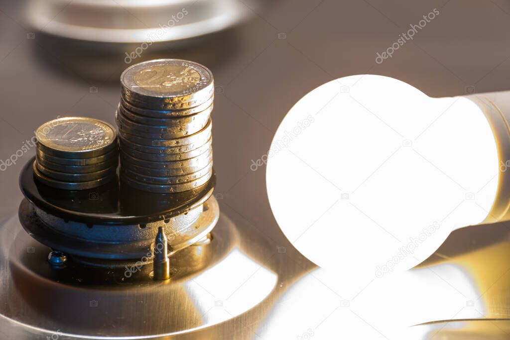 Light bulb on next to lit gas cooker, with coins next to it. Energy and gas costs, cost increases.