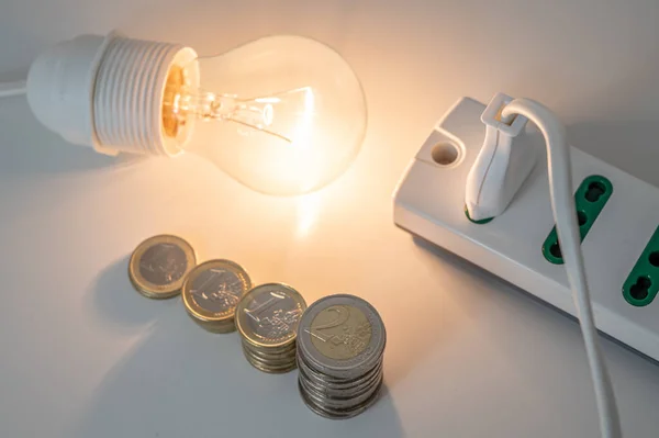 Light bulb on, with coins and a socket and plug next to it. Increase in electricity tariffs.