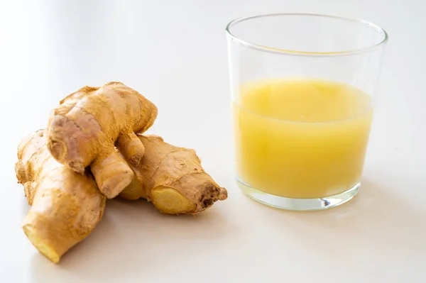 Ginger root, with pieces of ginger next to it and a glass of ginger juice.