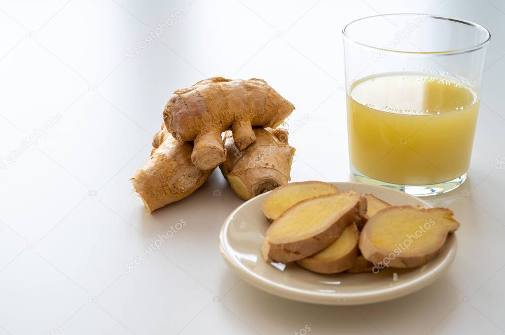 Ginger root, with pieces of ginger next to it and a glass of ginger juice. 
