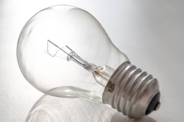 Beyaz bir yüzeyde, parlak bir ampul, ışığa karşı fotoğraflandı. Elektrik ve ışıklandırma maliyeti. Aydınlatma aygıtları.