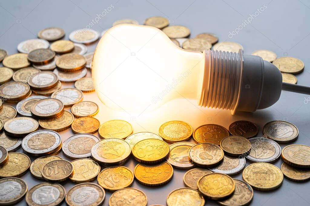 Light bulb turned on, with coins around. Increase in electricity tariffs, energy dependence, energy sources and energy supplies. 