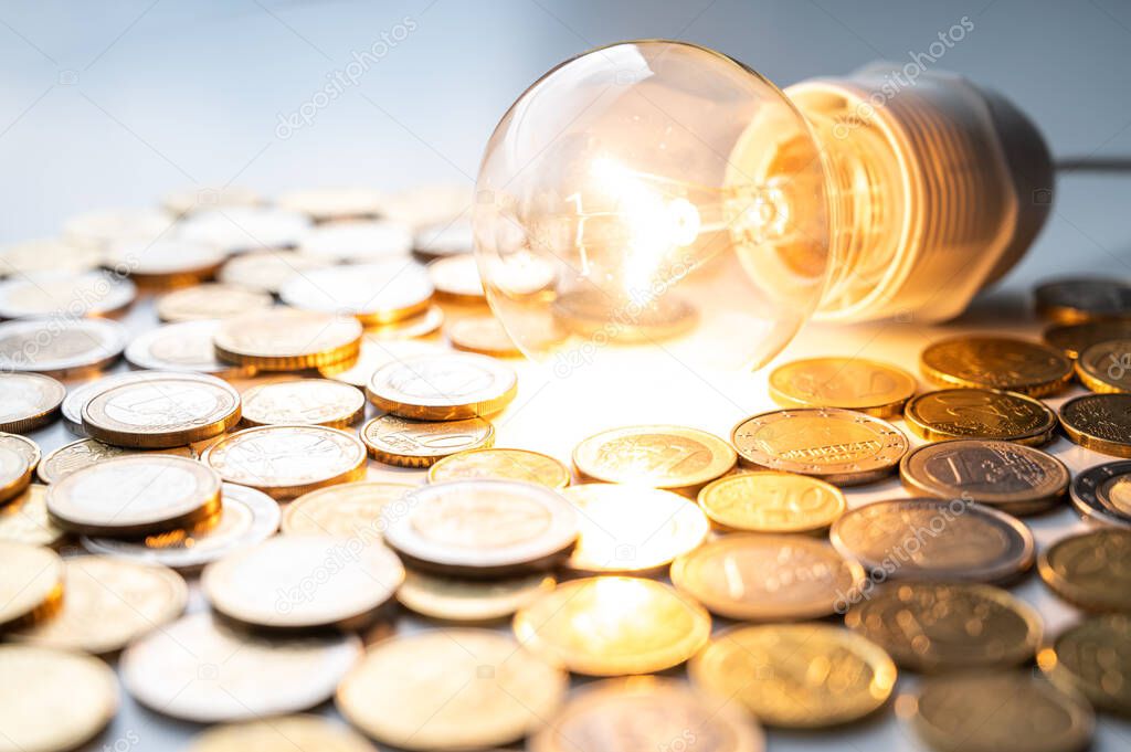 Light bulb turned on, with coins around. Increase in electricity tariffs, energy dependence, energy sources and energy supplies. 